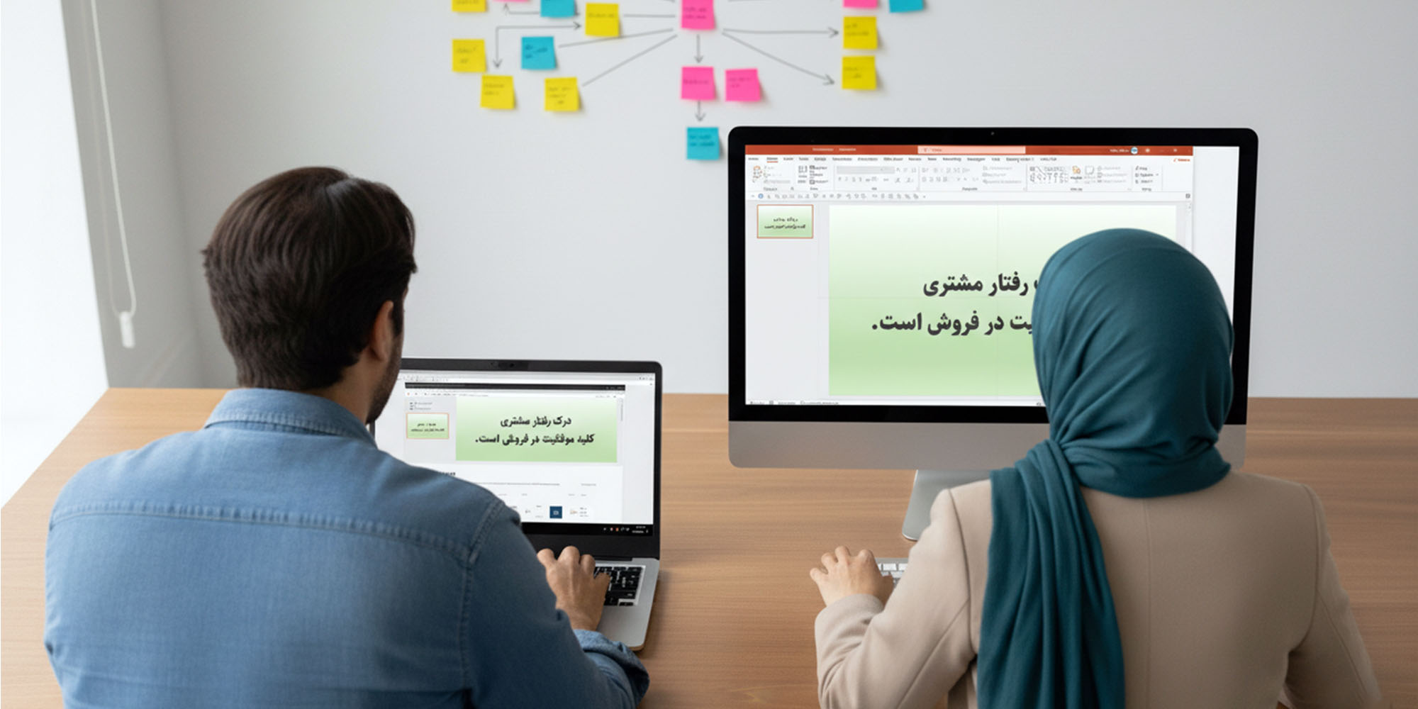 یک مرد و یک زن در حال کار روی طرح نهایی اسلایدهای یک ارائه (Presentation Slides) هستند. زن در حال استفاده از یک مانیتور کامپیوتر بزرگ و مرد در حال کار با لپ‌تاپ است. روی هر دو صفحه نمایش، یک اسلاید پاورپوینت با زمینه سبز کم‌رنگ و متنی به فارسی با عنوان "درک رفتار مشتری، کلید موفقیت در فروش است" دیده می‌شود. در پشت سر آن‌ها، روی دیوار، یک نقشه ذهنی با یادداشت‌های استیکی چسبانده شده است که مراحل قبلی طوفان فکری را نشان می‌دهد. این تصویر نشان‌دهنده اجرای طرح استوری‌بورد و آماده‌سازی نهایی اسلایدها است.