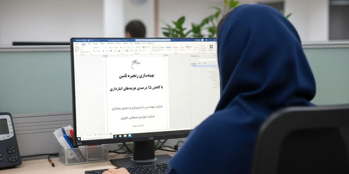 نمای پشت سر زنی را نشان می‌دهد که پشت میز اداری نشسته و در حال کار با کامپیوتر است. صفحه نمایش، متنی را در نرم‌افزار Word به زبان فارسی نشان می‌دهد که مربوط به یک مقاله، گزارش یا پروپوزال با عنوان "بهینه‌سازی زنجیره تأمین با کاهش ۱۵ درصدی هزینه‌های انبارداری" است. بخش کوچکی از میز و لوازم التحریر او در گوشه پایین سمت چپ قابل مشاهده است.