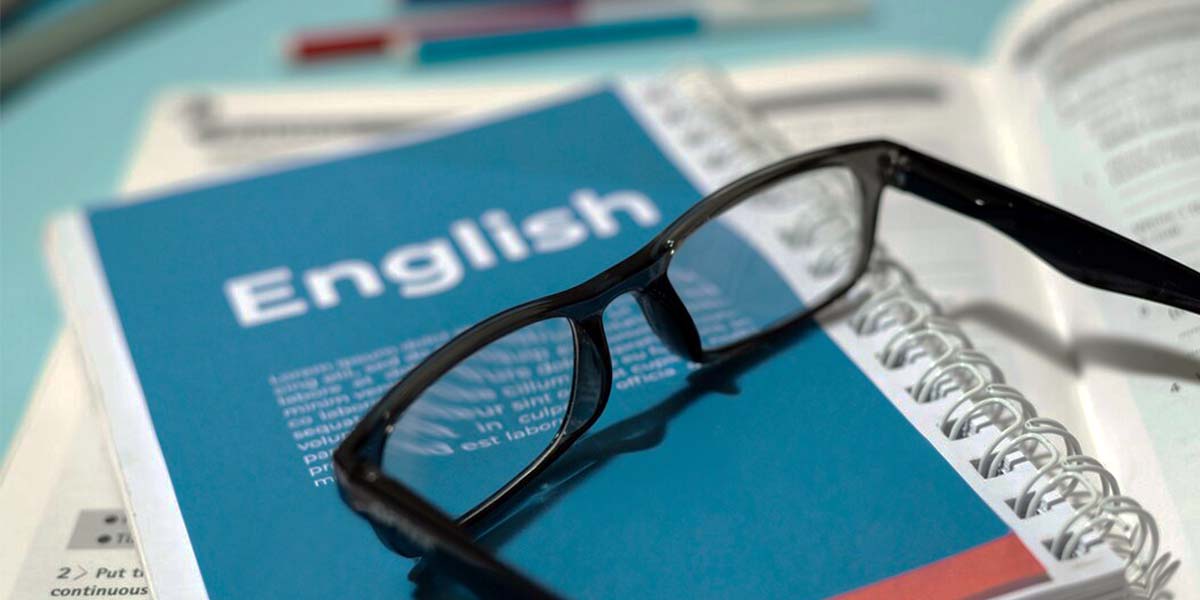 تصویر یک جزوه یا کتاب آموزشی با عنوان "English" به همراه یک عینک مطالعه که روی آن قرار گرفته، نمادی از تمرکز، مطالعه عمیق و آمادگی زبان برای نگارش علمی به زبان انگلیسی در فرآیند نوشتن پایان‌نامه است.